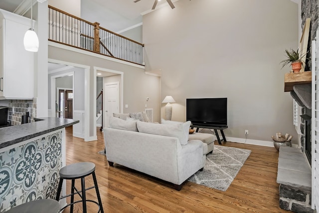 living room with ornamental molding, ceiling fan, a towering ceiling, and hardwood / wood-style floors