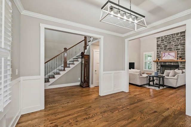 interior space with crown molding, dark wood-type flooring, a notable chandelier, and a stone fireplace