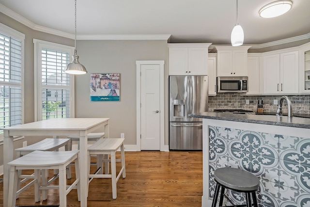 kitchen with ornamental molding, white cabinetry, hanging light fixtures, appliances with stainless steel finishes, and light hardwood / wood-style floors