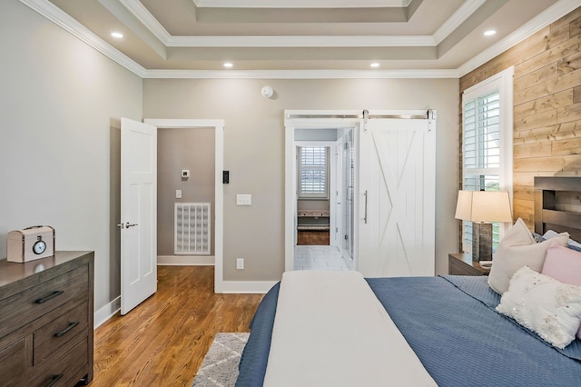 bedroom featuring crown molding, wood-type flooring, a tray ceiling, and a barn door