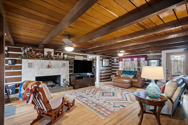 living room featuring beamed ceiling, hardwood / wood-style floors, ceiling fan, and a stone fireplace