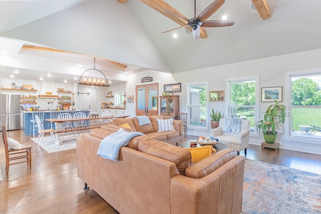 living room with high vaulted ceiling, ceiling fan with notable chandelier, hardwood / wood-style flooring, and beamed ceiling