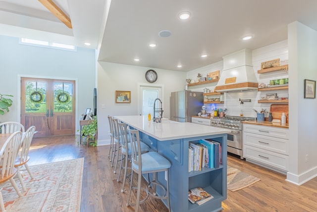 kitchen with a center island with sink, a breakfast bar, stainless steel appliances, custom exhaust hood, and white cabinets