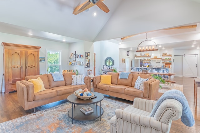 living room featuring ceiling fan with notable chandelier, high vaulted ceiling, hardwood / wood-style floors, and a barn door