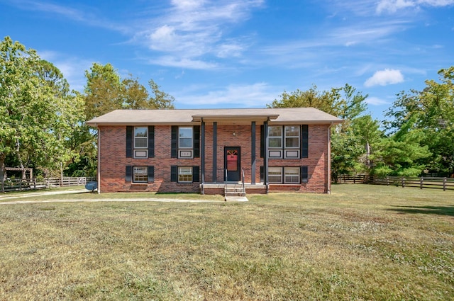 raised ranch with brick siding, a front lawn, and fence