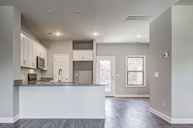 kitchen with white cabinets, kitchen peninsula, dark hardwood / wood-style floors, appliances with stainless steel finishes, and dark stone countertops