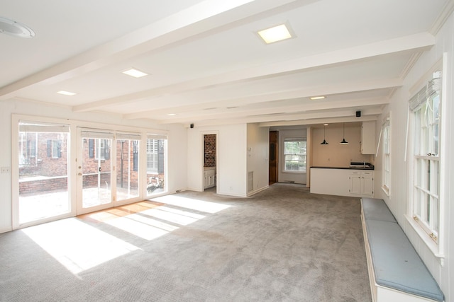 unfurnished living room with beam ceiling, light colored carpet, and a healthy amount of sunlight