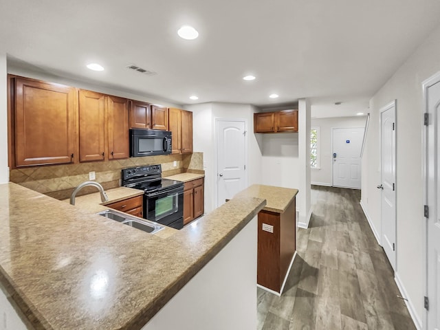 kitchen featuring a peninsula, a sink, brown cabinets, decorative backsplash, and black appliances