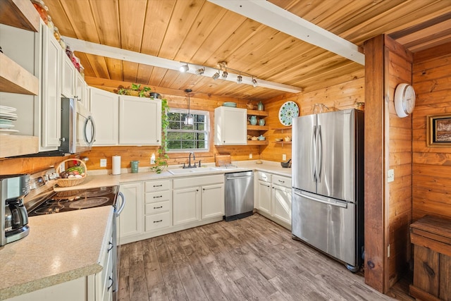 kitchen featuring white cabinets, appliances with stainless steel finishes, sink, light hardwood / wood-style floors, and wooden walls