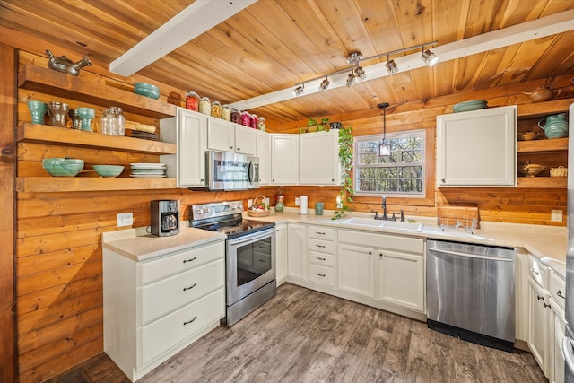 kitchen with white cabinets, hanging light fixtures, wood walls, sink, and stainless steel appliances