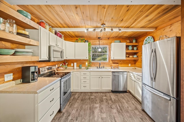 kitchen with white cabinetry, light hardwood / wood-style flooring, wood walls, sink, and stainless steel appliances