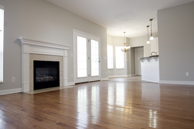 unfurnished living room featuring wood-type flooring, an inviting chandelier, and a high end fireplace