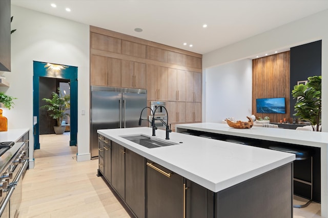 kitchen with a center island with sink, high end appliances, light countertops, light wood-type flooring, and a sink