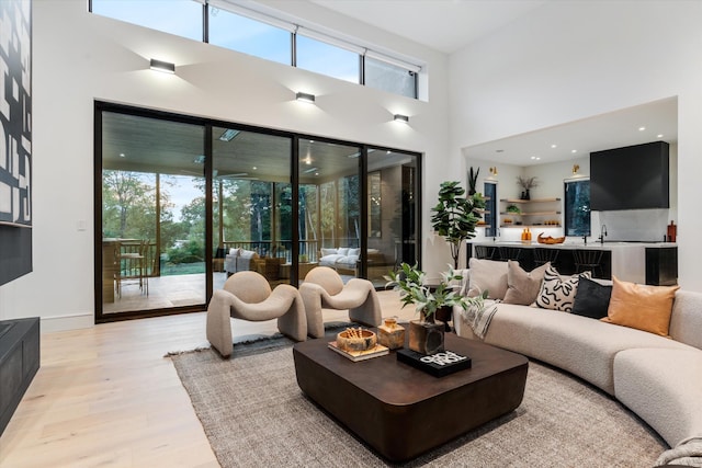 living room featuring a healthy amount of sunlight, light wood-style flooring, a high ceiling, and baseboards