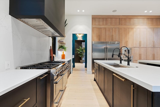 kitchen with range with two ovens, light countertops, a sink, and wall chimney exhaust hood