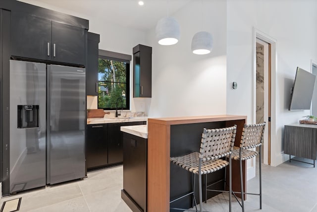 kitchen with a breakfast bar area, light countertops, dark cabinetry, stainless steel refrigerator with ice dispenser, and a sink