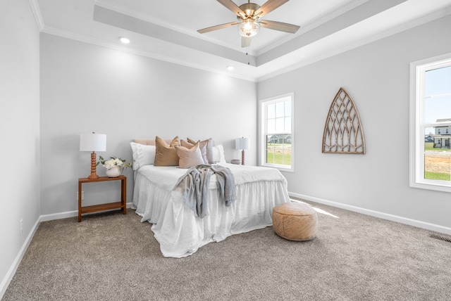 carpeted bedroom with ceiling fan, a raised ceiling, crown molding, and multiple windows