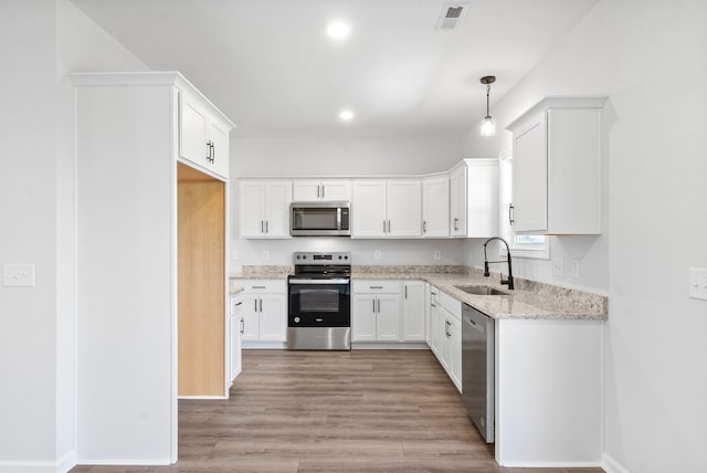 kitchen featuring stainless steel appliances, white cabinets, sink, pendant lighting, and light hardwood / wood-style flooring