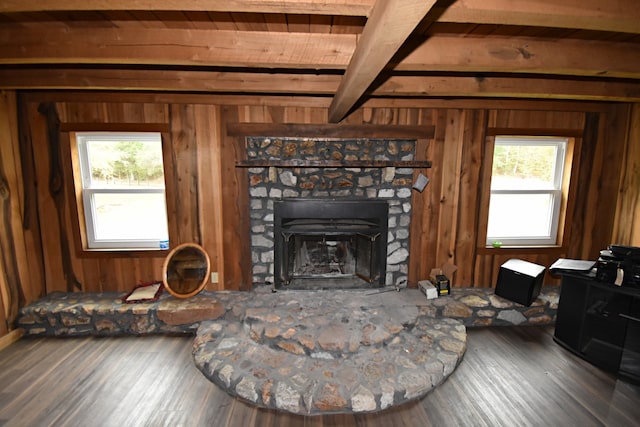 living room featuring wood-type flooring, a stone fireplace, beamed ceiling, and plenty of natural light