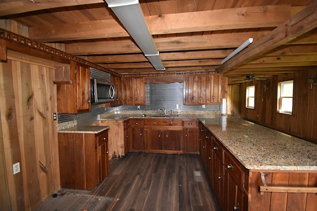 kitchen featuring sink, beam ceiling, wooden walls, light stone countertops, and dark hardwood / wood-style flooring