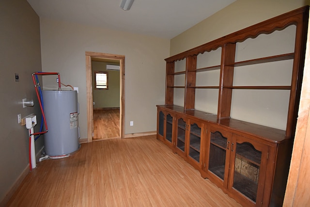 interior space with light hardwood / wood-style flooring, a wall unit AC, and electric water heater