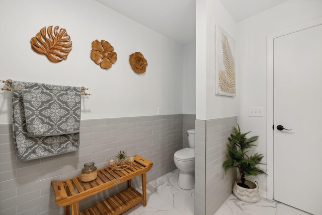 bathroom featuring marble finish floor, wainscoting, and toilet