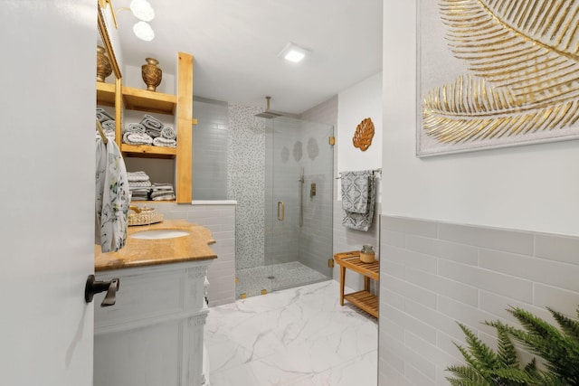 full bathroom featuring a wainscoted wall, vanity, tile walls, marble finish floor, and a stall shower