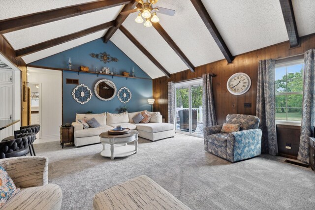 carpeted living room featuring a textured ceiling, ceiling fan, wooden walls, and vaulted ceiling with beams