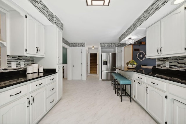 kitchen with dark countertops, white cabinets, backsplash, and stainless steel fridge with ice dispenser