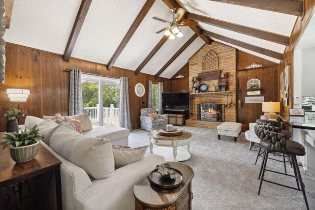 carpeted living room featuring ceiling fan, lofted ceiling with beams, wooden walls, and a fireplace