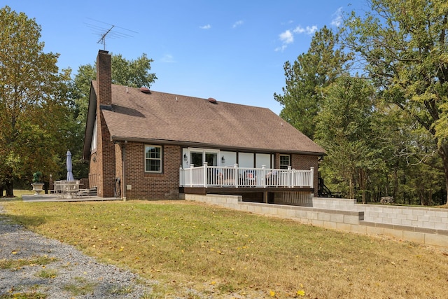 rear view of property with a wooden deck, a shingled roof, a chimney, a yard, and brick siding