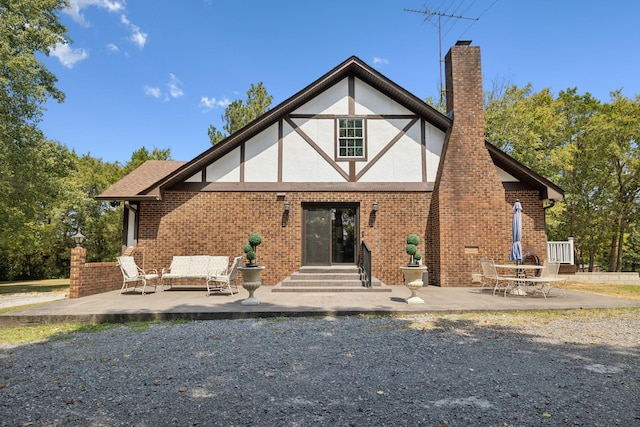 back of house with entry steps, brick siding, a chimney, and a patio area