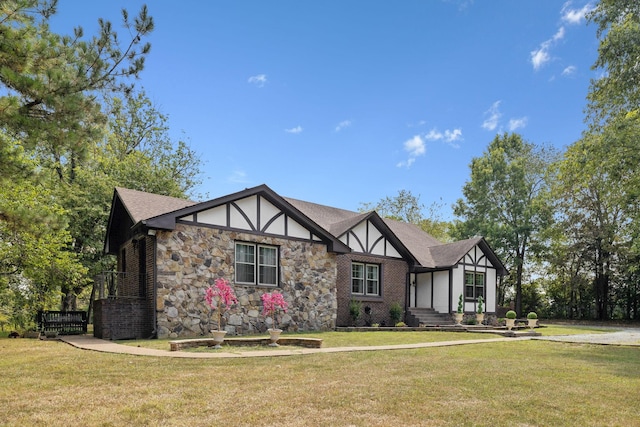 tudor home featuring brick siding, roof with shingles, and a front yard