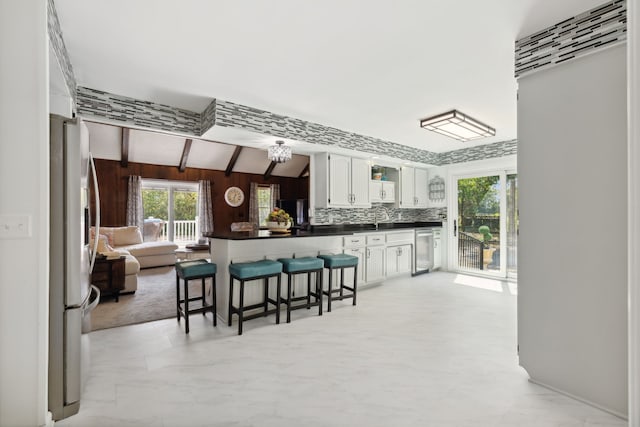 kitchen featuring white cabinets, stainless steel fridge, a breakfast bar area, decorative backsplash, and vaulted ceiling with beams