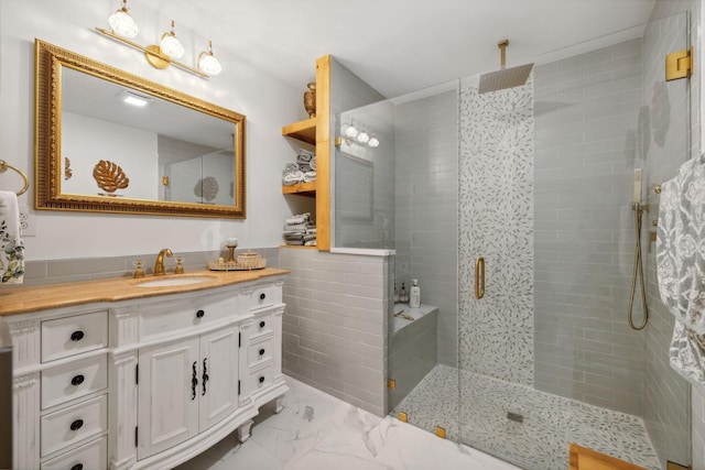 full bathroom featuring marble finish floor, vanity, a tile shower, and tile walls