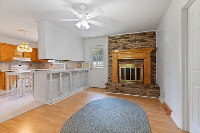 kitchen featuring light wood-type flooring, a brick fireplace, decorative light fixtures, and ceiling fan