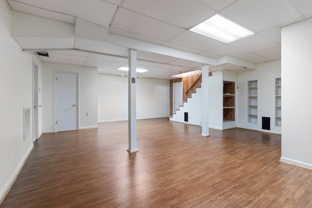 basement with built in features, a paneled ceiling, and hardwood / wood-style flooring