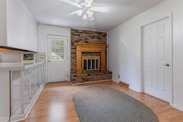 living room featuring light wood-type flooring, ceiling fan, and a brick fireplace