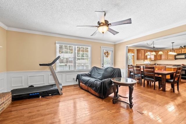 workout area featuring ceiling fan, a textured ceiling, crown molding, and light hardwood / wood-style flooring