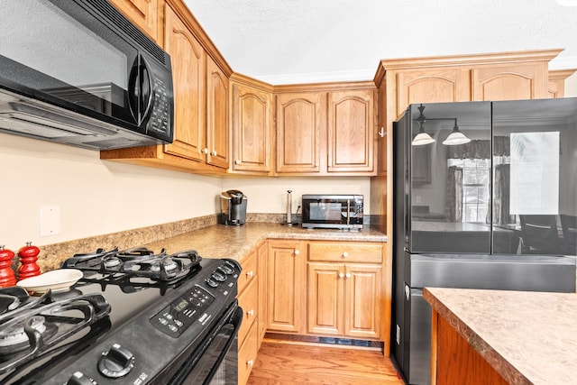 kitchen featuring light wood-type flooring, black appliances, and a textured ceiling