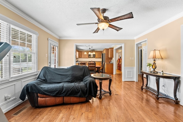 living room with ceiling fan with notable chandelier, crown molding, a textured ceiling, and light hardwood / wood-style flooring