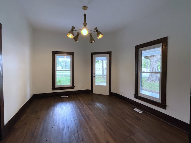 spare room featuring dark hardwood / wood-style flooring, a healthy amount of sunlight, and an inviting chandelier