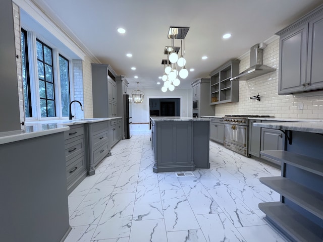 kitchen featuring gray cabinetry, a notable chandelier, a center island, high end range, and wall chimney range hood