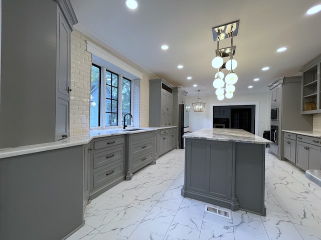 kitchen with an inviting chandelier, pendant lighting, appliances with stainless steel finishes, sink, and gray cabinets