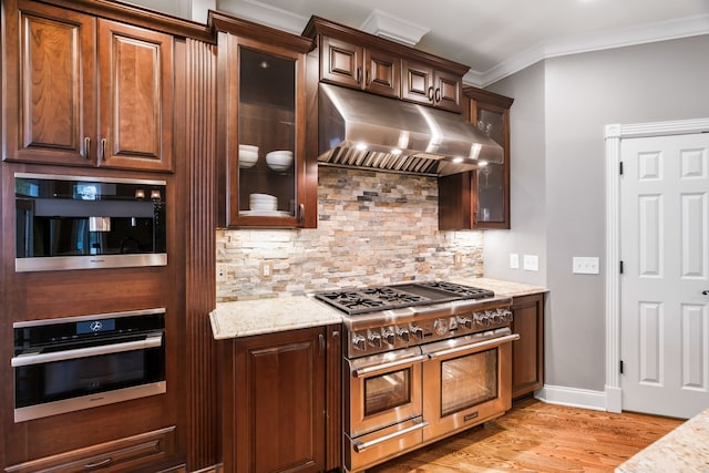 kitchen with light wood-type flooring, ornamental molding, tasteful backsplash, light stone counters, and appliances with stainless steel finishes