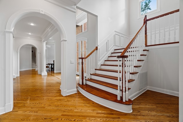 stairway with ornamental molding, a towering ceiling, and hardwood / wood-style floors