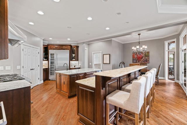 kitchen with light hardwood / wood-style flooring, crown molding, a kitchen island with sink, and a breakfast bar