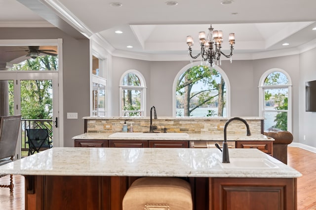 kitchen featuring a center island with sink, a healthy amount of sunlight, light stone counters, and tasteful backsplash