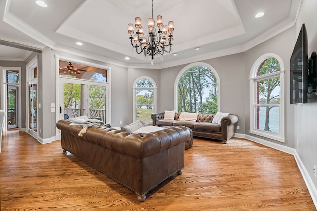 living room with ornamental molding, a raised ceiling, a notable chandelier, and light hardwood / wood-style floors