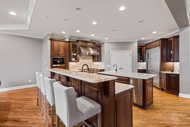 kitchen featuring a breakfast bar area, light hardwood / wood-style flooring, appliances with stainless steel finishes, an island with sink, and decorative backsplash